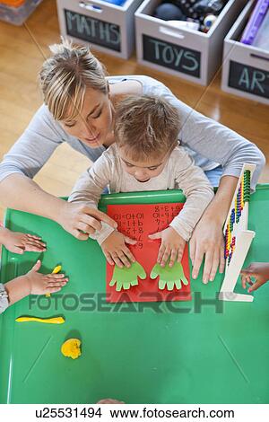 Picture - Overhead view of teacher and pupils counting with fingers at nursery school. Fotosearch