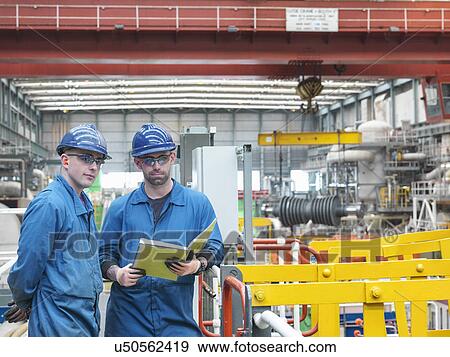 Stock Photo - Portrait of engineers discussing notes on walkway during power station outage. Fotosearch