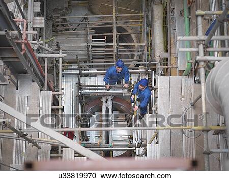 Stock Image - Portrait of engineers working deep down in equipment during power station outage, high angle view. Fotosearch