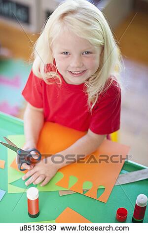 Stock Photo - Portrait of girl cutting shapes at nursery school. Fotosearch