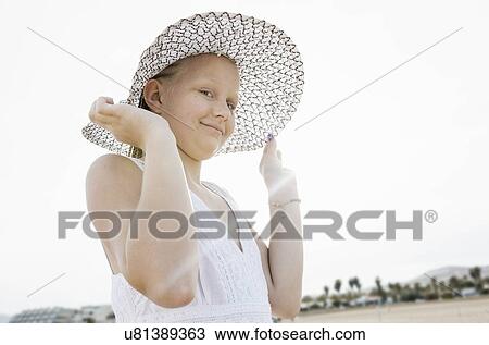 Stock Image - Portrait of girl holding her sunhat on beach. Fotosearch