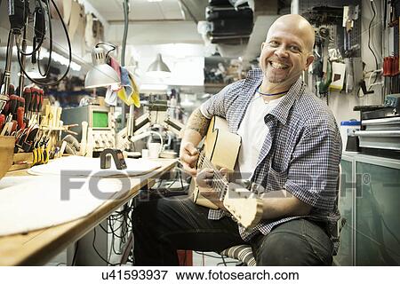 Stock Photo - Portrait of guitar maker tuning acoustic guitar in workshop. Fotosearch