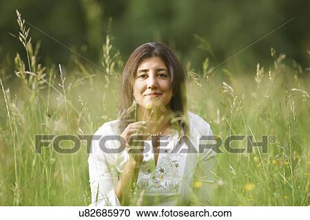 Stock Image - Portrait of mature woman in long grass holding buttercup. Fotosearch
