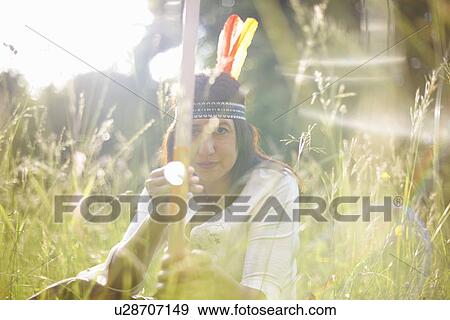 Stock Photo - Portrait of mature woman in long grass holding bow and arrow. Fotosearch