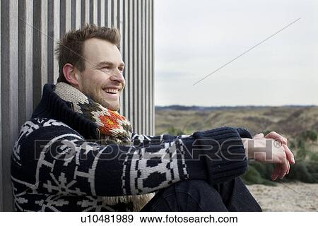 Stock Photo - Portrait of mid adult man leaning against corrugated building at coast. Fotosearch