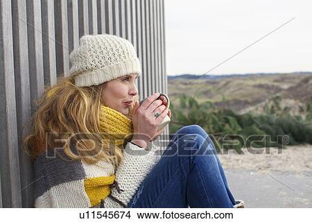 Picture - Portrait of mid adult woman leaning against corrugated building at coast. Fotosearch