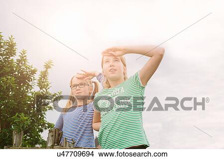 Picture - Portrait of nine year old girl and sister shielding eyes in field. Fotosearch