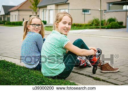Stock Image - Portrait of nine year old girl and sister putting on rollerblades on sidewalk. Fotosearch