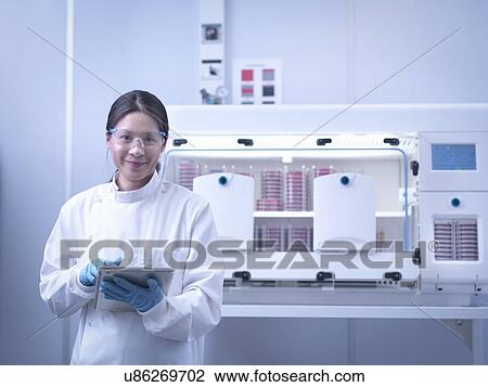 Stock Image - Portrait of scientist with bacterial cultures inside laboratory workstation. Fotosearch
