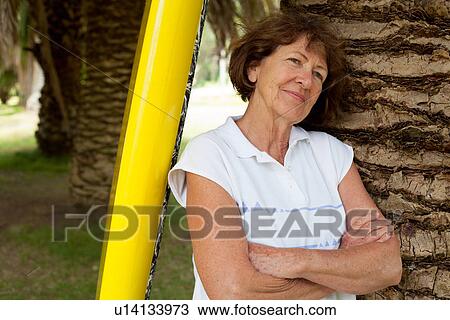 Portrait of senior woman leaning against palm tree in park View Large Photo Image Stock Image - Portrait of senior woman leaning against palm tree in park. Fotosearch