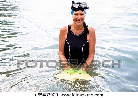 Stock Image - Portrait of senior woman snorkeler holding flippers in sea. Fotosearch