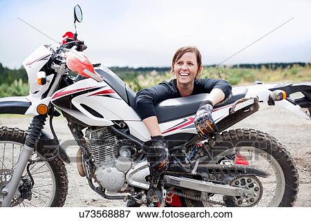 Stock Photo - Portrait of smiling young adult female motorcyclist with motorcycle. Fotosearch
