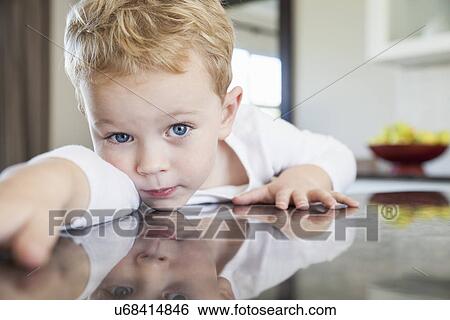 Stock Photograph - Portrait of three year old boy leaning forward on kitchen bench. Fotosearch