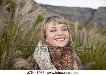Stock Photography - Portrait of young woman amongst long grass with eyes closed. Fotosearch