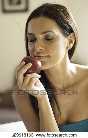 Stock Image - Portrait of young woman smelling red apple. Fotosearch