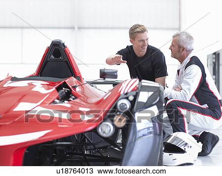 Stock Image - Racing car driver and engineer with supercar in sports car factory. Fotosearch