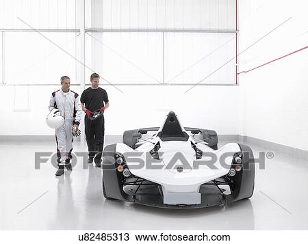 Stock Image - Racing driver with engineer and supercar in car factory. Fotosearch