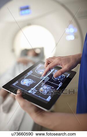 Stock Image - Radiographer looking at brain scan image on digital tablet. Fotosearch