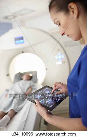 Stock Photograph - Radiographer looking at brain scan image on digital tablet. Fotosearch