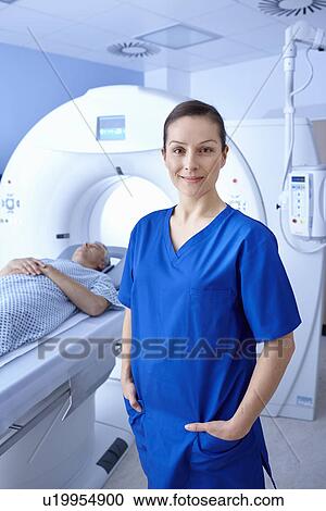 Stock Image - Radiographer standing in front of man going into CT scanner. Fotosearch