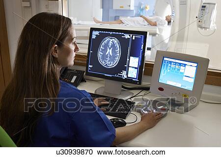 Stock Image - Radiologist looking at brain scan image on computer screen. Fotosearch