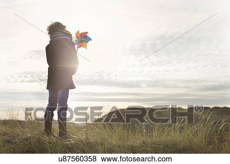 Rear view of boy holding up paper windmill at coast View Large Photo Image Stock Photo - Rear view of boy holding up paper windmill at coast. Fotosearch