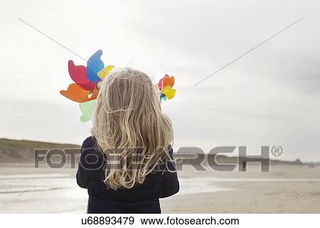 Stock Photo - Rear view of girl with paper windmills on beach, Bloemendaal aan Zee, Netherlands. Fotosearch