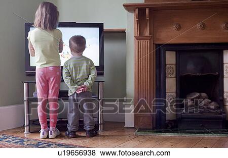 Stock Photo - Rear view of sister and brother standing too close to and watching TV. Fotosearch