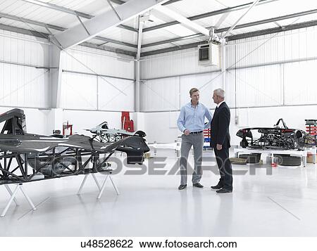 Stock Image - Salesman discussing supercar with customer in factory. Fotosearch