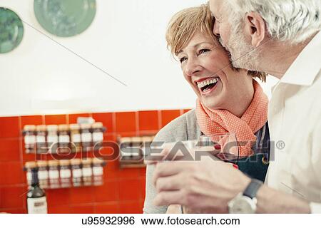 Senior man kissing woman in kitchen, woman laughing View Large Photo Image Stock Photograph - Senior man kissing woman in kitchen, woman laughing. Fotosearch