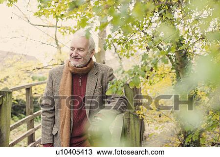 Stock Image - Senior man leaning on wooden fence, smiling. Fotosearch