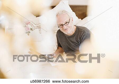Stock Photograph - Senior man reading newspaper, smiling. Fotosearch