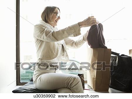 Stock Image - Senior woman admiring purchases in shop window seat. Fotosearch