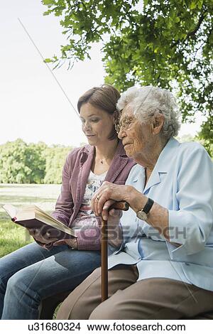 Senior woman and granddaughter sitting on park bench reading bible View Large Photo Image Picture - Senior woman and granddaughter sitting on park bench reading bible. Fotosearch