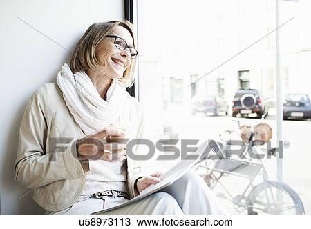 Stock Image - Senior woman having a coffee in cafe window seat. Fotosearch