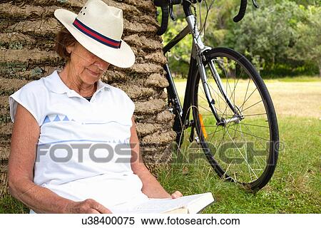Senior woman leaning against palm tree reading in park View Large Photo Image Stock Photography - Senior woman leaning against palm tree reading in park. Fotosearch