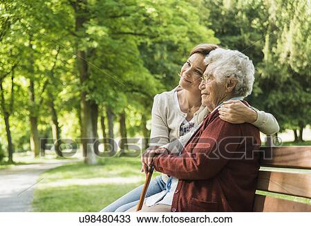 Stock Image - Senior woman sitting on park bench with granddaughter. Fotosearch