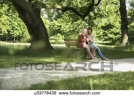 Senior woman sitting on park bench with granddaughter View Large Photo Image Stock Photo - Senior woman sitting on park bench with granddaughter. Fotosearch