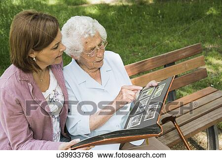 Senior woman sitting on park bench with granddaughter, looking at old photograph album View Large Photo Image Stock Photo - Senior woman sitting on park bench with granddaughter, looking at old photograph album. Fotosearch