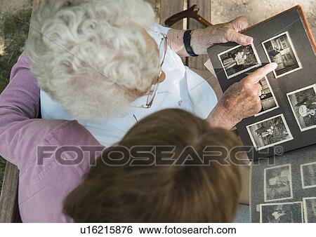 Stock Photograph - Senior woman sitting on park bench with granddaughter, looking at old photograph album. Fotosearch