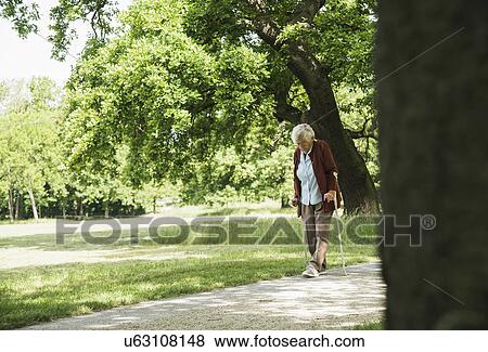 Senior woman walking through park, using walking stick View Large Photo Image Stock Photo - Senior woman walking through park, using walking stick. Fotosearch