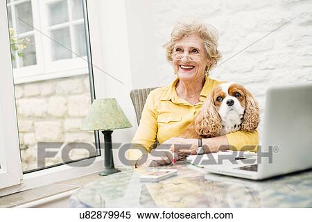 Stock Photography - Senior woman with dog, using laptop. Fotosearch