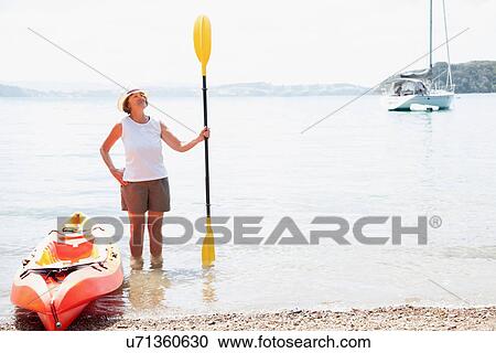 Stock Image - Senior woman with paddle and sea kayak. Fotosearch