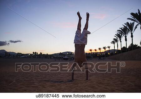 Stock Photography - Silhouetted boy doing handstand on beach at dusk. Fotosearch