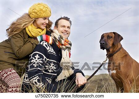 Stock Photography - Smiling mid adult couple and dog at coast. Fotosearch