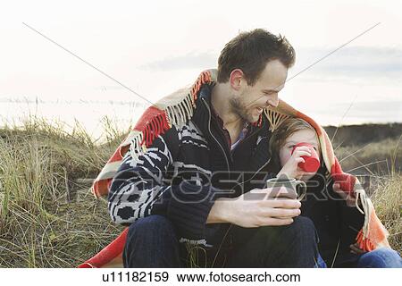 Smiling mid adult man and son wrapped in blanket on sand dunes View Large Photo Image Stock Photo - Smiling mid adult man and son wrapped in blanket on sand dunes. Fotosearch