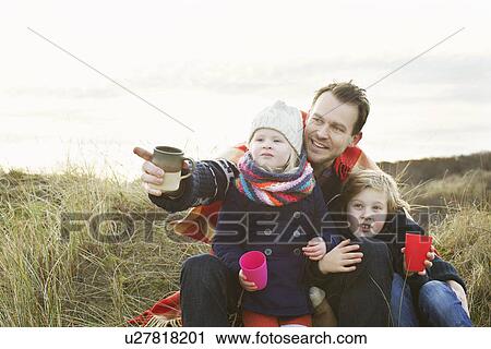 Stock Image - Smiling mid adult man with daughter and son on sand dunes. Fotosearch