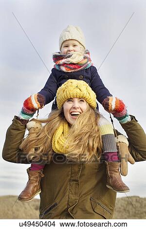 Picture - Smiling mid adult woman carrying daughter on shoulders at coast. Fotosearch