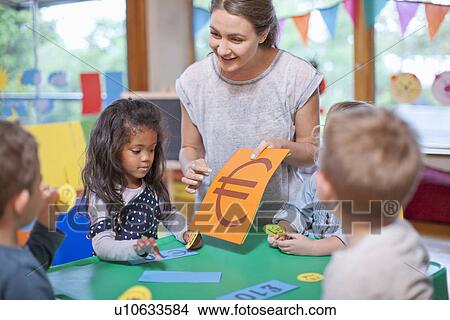 Picture - Teacher and pupils counting euro currency at nursery school. Fotosearch