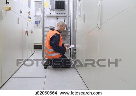 Picture - Technician reading paperwork in power station control room. Fotosearch